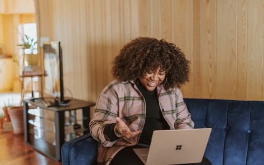 Image of woman sat on a sofa with a laptop on her lap, smiling